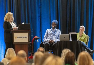 Speakers on stage being introduced by woman at podium