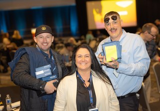 Three team members showing off a stack of awards