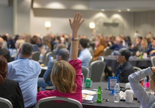 A woman in pink raising her hand in a conference room