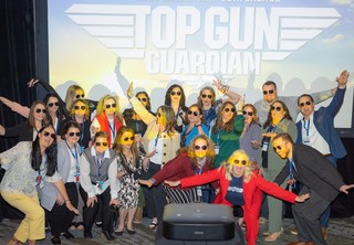 Group of professionals in front of a Top Gun sign, posing with their arms in flight mode