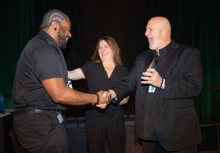 A woman and a man giving another man an award on stage