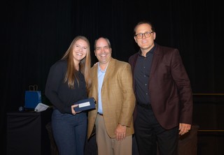 A woman posing with her award with two men