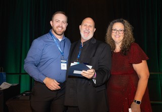 Three individuals posing on stage with an award