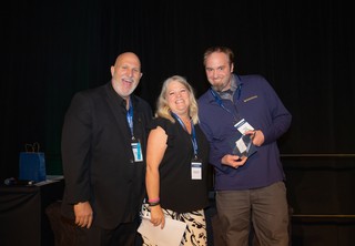 Three individuals on stage celebrating an award
