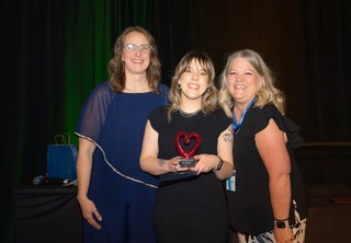 Three women posing with a heart award