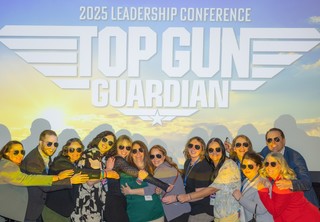 Group of professionals wearing aviator sunglasses hugging and posing in front of a Top Gun sign