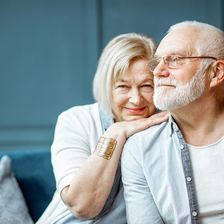 Senior women embracing senior man sitting on couch