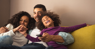 Family of three on couch laughing and watching tv