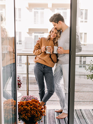 Couple embracing on balcony of apartment building with coffee