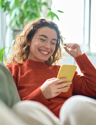 Woman smiling and sitting on couch and looking at phone
