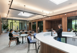 Co-working space with balcony, tables, and counter bar, with a woman pouring kombucha