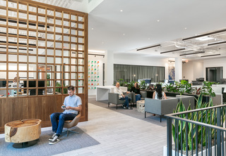 Office entrance with man waiting and open working area with professionals talking